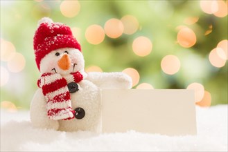 Cute snowman with scarf and hat next to blank white card over abstract background