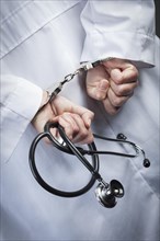 Female doctor or nurse in handcuffs and lab coat holding stethoscope