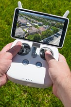 Hands holding drone quadcopter controller with residential homes on screen