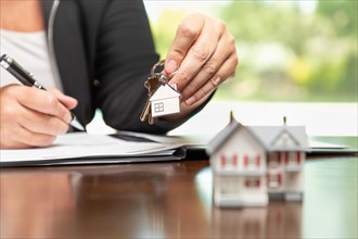 Woman signing real estate contract papers holding house keys and home keychain with small model home in front