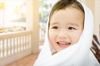 Happy cute mixed-race chinese and caucasian boy on tropical patio wrapped in A towel