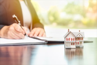 Woman signing real estate contract papers with small model home in front