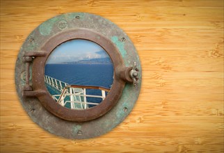 Antique porthole on bamboo wall with view of ship deck railing