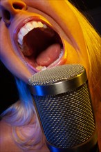 Female vocalist under gelled lighting sings with passion into condenser microphone