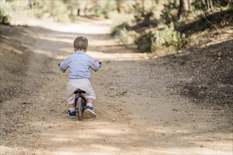 Back of cute toddler riding bicycle on dirt road in forest