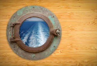Antique porthole on bamboo wall with view of ship wave trail