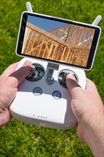 Hands holding drone quadcopter controller with construction house framing on screen