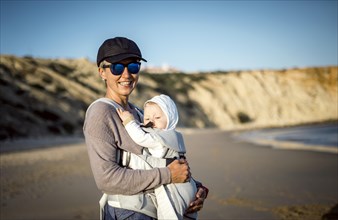 A mother with his son in the carrier on the beach in Portugal