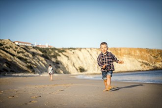 The small boy happily running on the beach by sunset