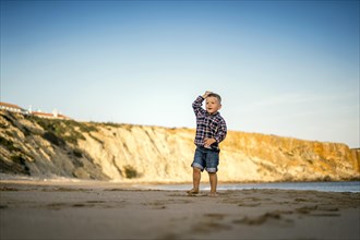 Small boy throwing stones on the beach by the sunset