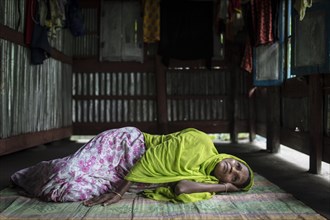 A woman lies on a carpet on the floor in her hut