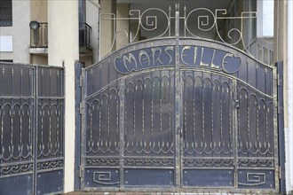 Iron gate with inscription MARSEILLE in front of a residential building on French Boulevard