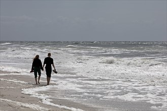 Young couple walking on the beach at the surf