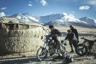 Two men push the motorcycle of a Kyrgyz nomad to get it running again