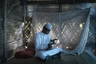 Ahmed on a raffia rug on the floor of a hut playing with two birds
