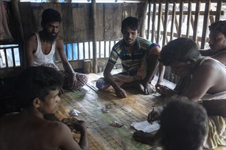 Six fishermen sit on the floor and play cards in a wooden hut