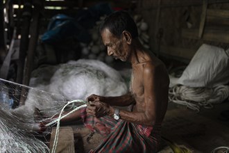 A fisherman sits on the floor of his hut repairing a fishing net