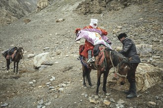 A man helps his pregnant woman onto a horse