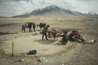 Two men load a donkey with components of a yurt in front of moving to winter camps