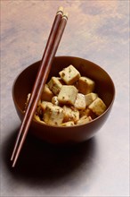 Fried tofu cubes with sesame seeds in bowl and chopsticks
