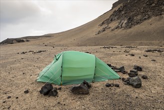 Green tent braced with lava rock