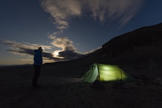 Man with headlamp standing in front of tent lit from inside