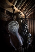 Old decorated saddle and bridle in horse stable in original peat construction