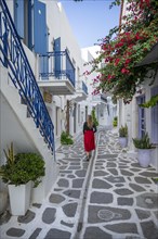 Young woman with dress walking through alley with Cycladic houses