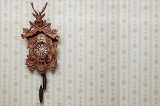 Old black forest cuckoo clock in front of old-fashioned wallpaper wall