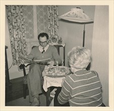 Christmas 1956: A married couple sits at a small table with a candle and Christmas biscuits on top