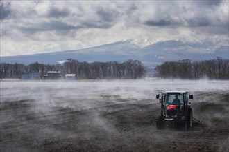Tractor seeding a field while it is vaporating from the warm ground