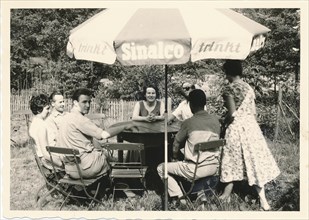 Southern Germany in 1959: Participants of a company outing sit in the beer garden of a pub under a parasol with advertising drinking Sinalco