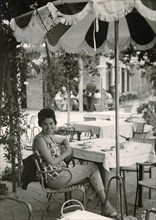 Lake Garda in 1960: young German tourist sitting under a parasol at a table of a restaurant at the harbour of Limone sul Garda