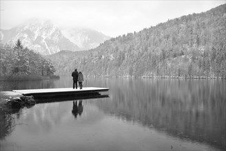 Lake with reflection and footbridge with two people in winter black and white