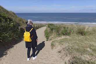 Senior woman with yellow backpack walking on path through dunes