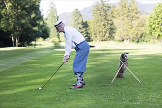 Older man in straw hat and knickerbockers playing hickory golf on a golf course
