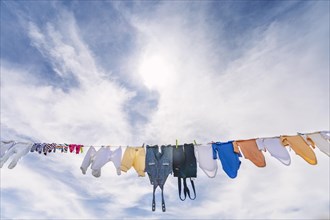 A lot of small baby clothes hanging against blue cloudy sky