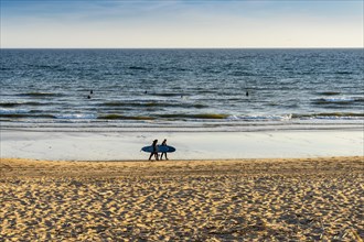 Surfers in the ocean and surfers walking on the beach in Faro