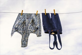Elegant baby trousers and shirt pinned with wooden pegs against cloudy sky