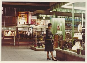 Stuttgart at night in 1963: A young woman with a coat and handbag looks at the display of handbags and suitcases in a leather goods shop