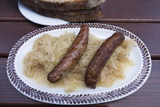 Two Nuremberg bratwursts with sauerkraut and bread on an oval plate in a garden restaurant
