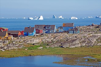 Wooden houses and rocks in front of a bay filled with icebergs