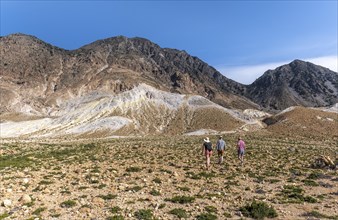 Three tourists hiking in a volcanic caldera with pumice fields