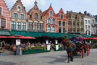 Horse-drawn carriage with tourists and guild houses with restaurants on the market square of Bruges