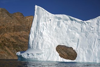 Iceberg with hole in front of barren mountains