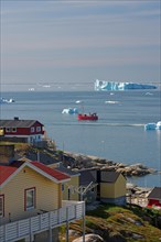 Wooden houses in front of a bay with fishing boat and icebergs