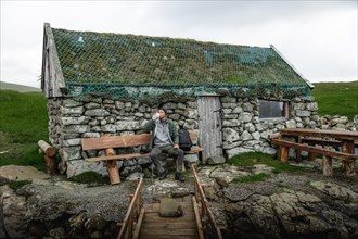 Hiker drinking water on a bench in front of a stone hut