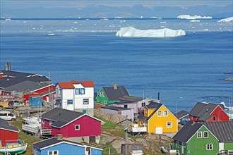 Wooden houses in different colours in front of bay with icebergs