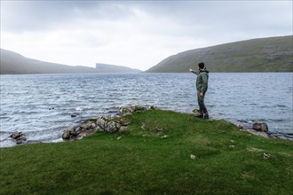Hiker standing on the shore of Lake Leitisvatn pointing into the distance