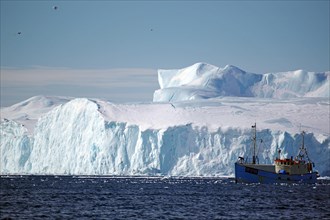 Small fishing boat in front of huge icebergs and drift ice